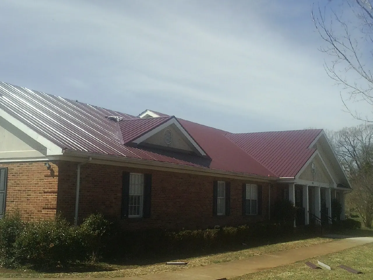 Red metal roof with gabled entries on a long brick building, from a Hail Damage Roof Repair job in Stone Park