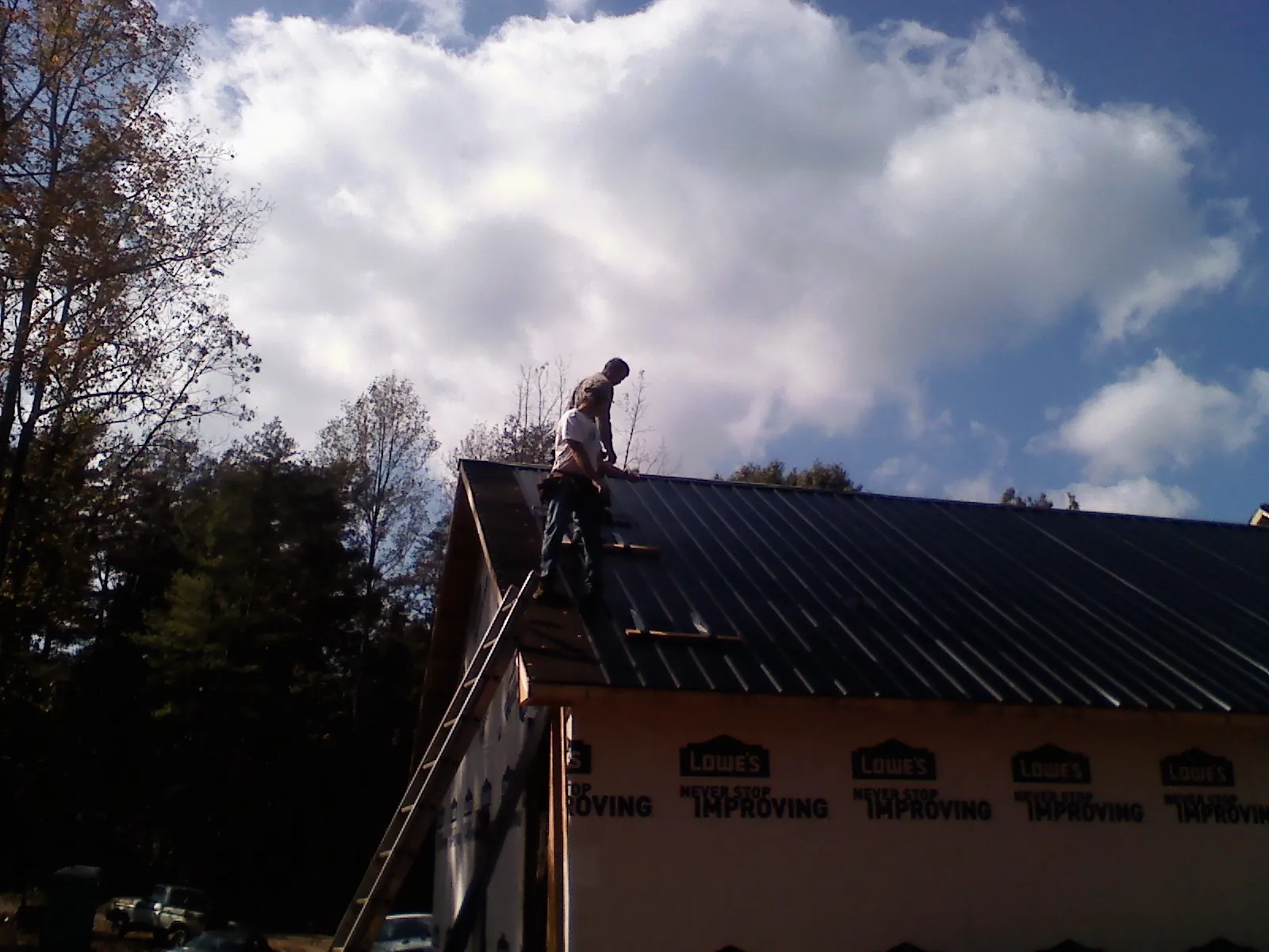 Roofer fastening dark metal panels high against a cloudy sky, from a Roof Inspection job in Stone Park