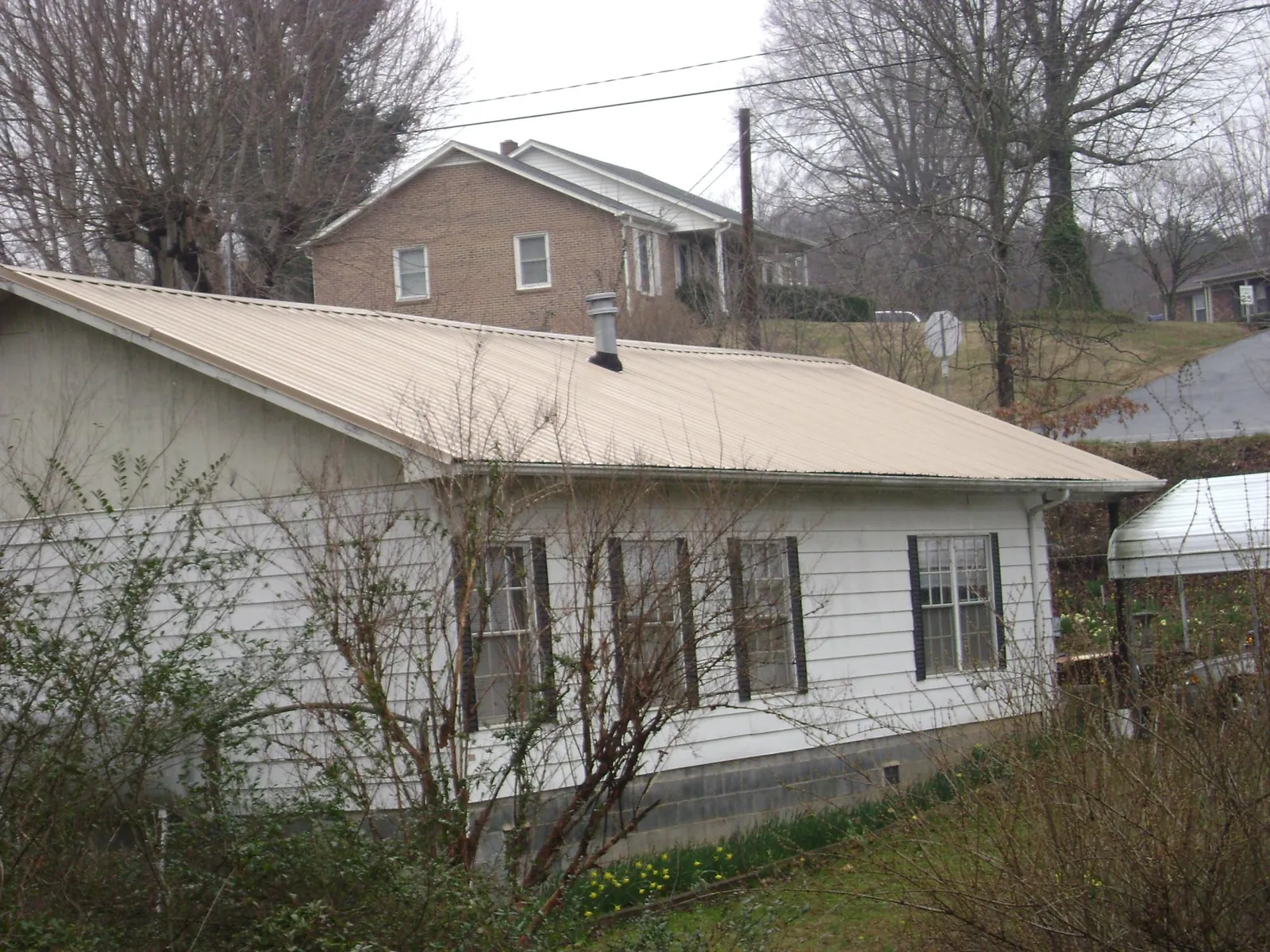 Tan metal roof on a white sided house set into a hillside — Commercial Roofing by Roofing Brothers in Stone Park